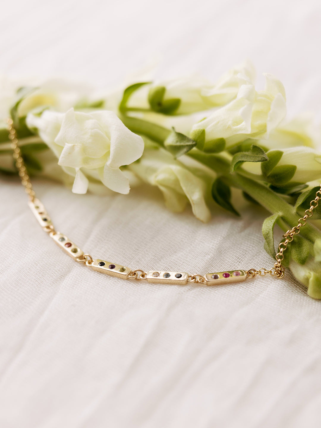 The Tribute Bracelet by Close By Me in 14K Yellow Gold on a light mesh fabric background. It has 5 bar links with 3 birthstones in each.