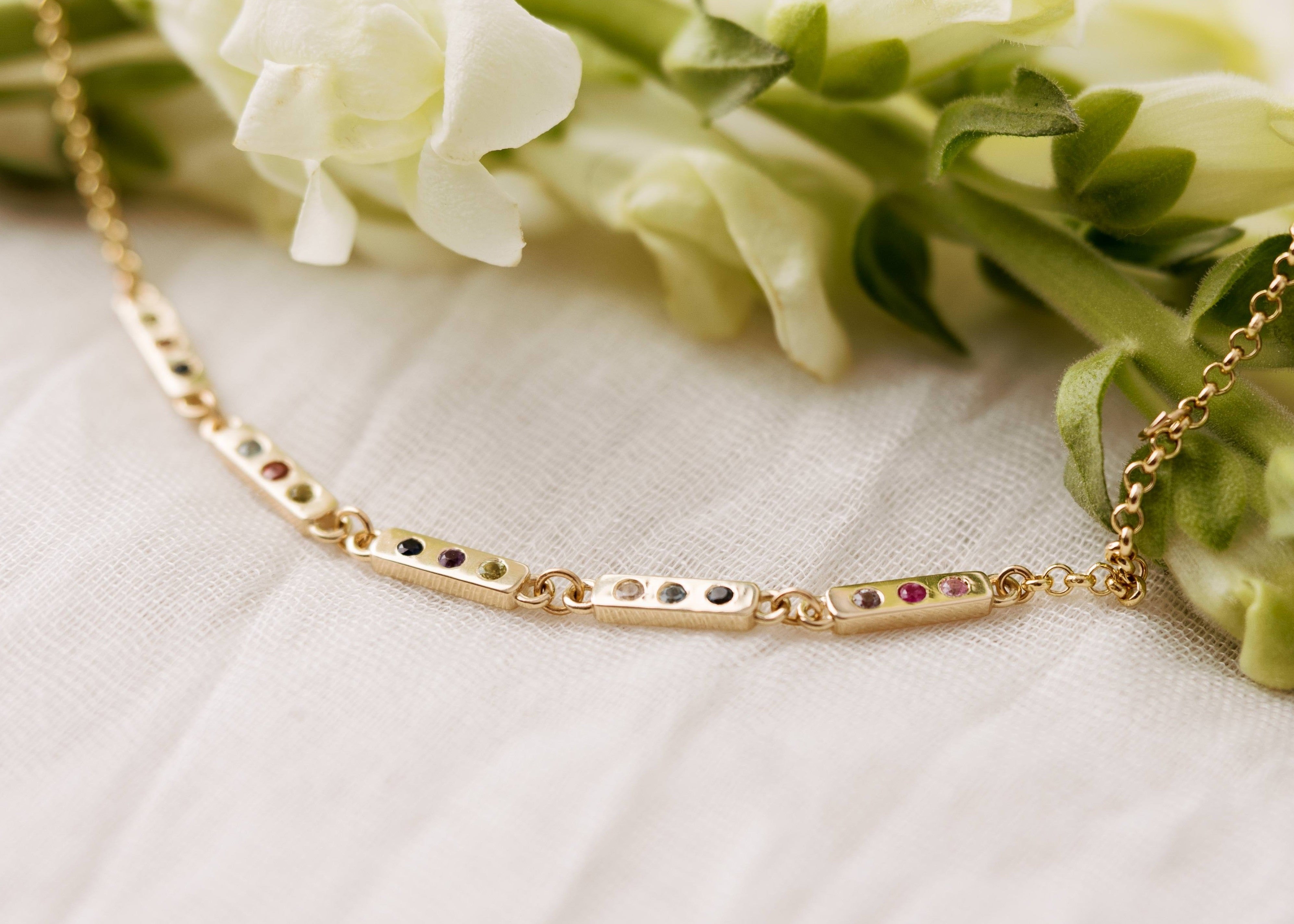 Solid 14k gold bracelet with birthstones on a white fabric background