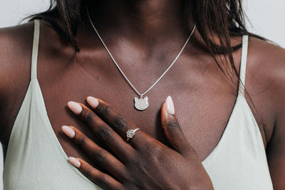 A model with dark skin in a light green dress wearing the Cat Necklace with cremains by close by me jewelry in sterling silver