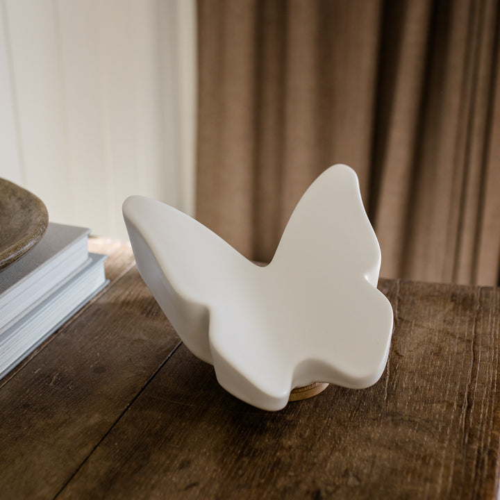 White ceramic butterfly cremation urn  on a wooden surface with a blurred curtain background