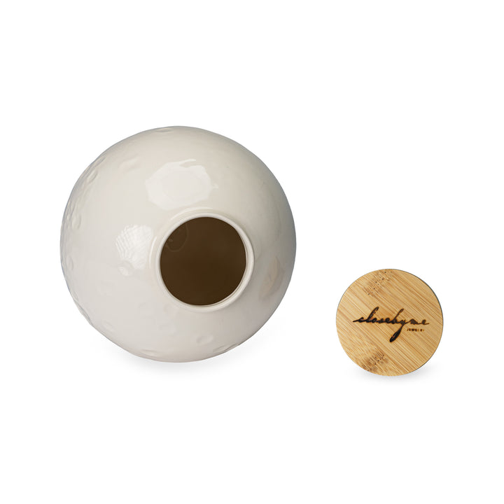 The open bottom of Close By Me's Ceramic Moon Keepsake Urn next to the logo-branded bamboo lid.