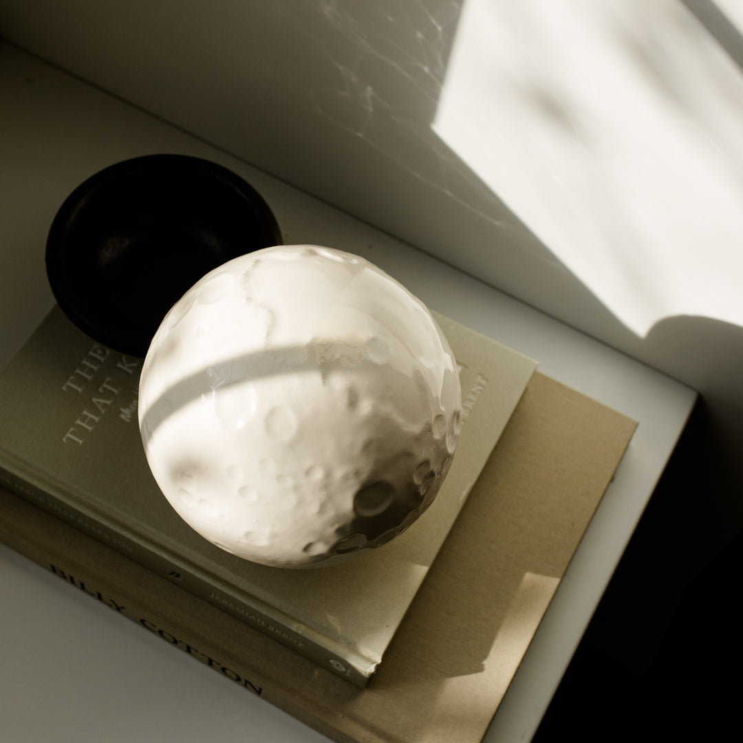 Overhead view of ceramic moon cremation urn on a stack of books