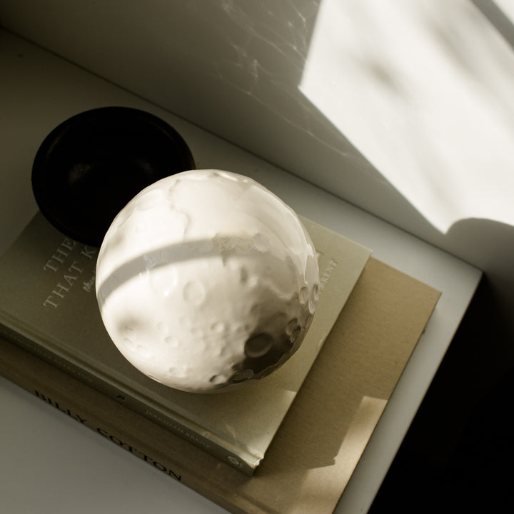 Overhead view of ceramic moon cremation urn on a stack of books