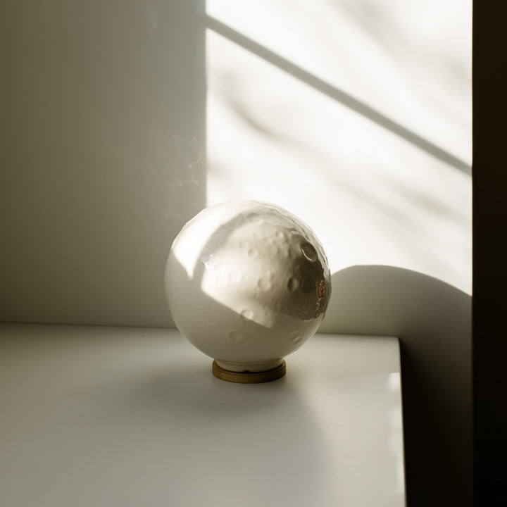Ceramic moon cremation urn on a white counter against a white wall with natural side lighting
