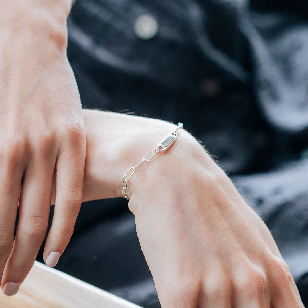 A close-up view, with bright lighting, of Close By Me's Chain Link Cremation Bracelet in Sterling Silver on the wrist of a female model.