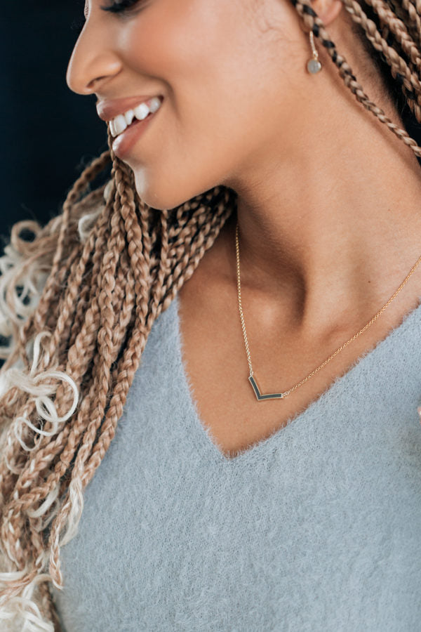 A model with blonde braids in a grey sweater wearing the chevron ashes necklace by close by me jewelry in 14k yellow gold