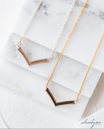 Both the sterling silver and 14k yellow gold versions of close by me jewelry's chevron memorial necklace lying flat against white marble