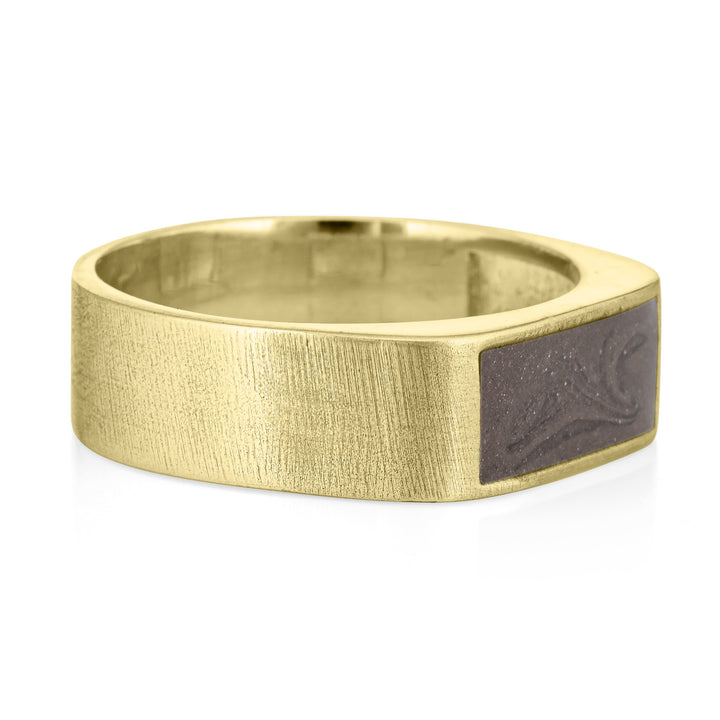 Pictured here is close by me jewelry's Men's Classic Band Cremation Ring design in 14K Yellow Gold from the side to show its dark grey ashes setting and thickness of its brushed band