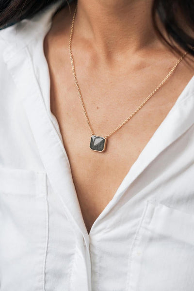 The 14k yellow gold cushion art deco cremation pendant designed and set with ashes by close by me jewelry being worn by a tan model in white button-down