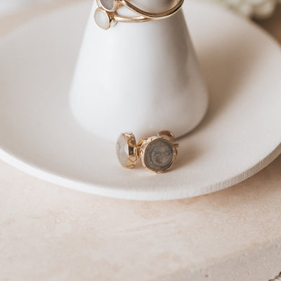 14k yellow gold stud cremation earrings shown laying on the bottom of a clay ring holder