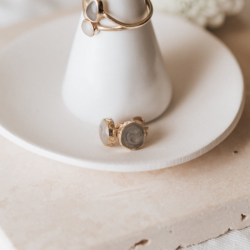 14k yellow gold detailed stud cremation earrings shown laying on the plate of a ring holder