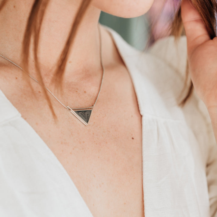A close up, angled shot of a model wearing a white dress and close by me jewelry's detailed sliding triangle pendant with ashes