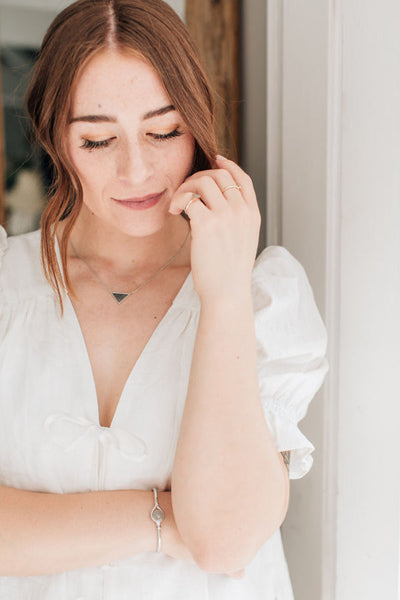 The sterling silver detailed sliding triangle cremation necklace being worn by a model in a white dress