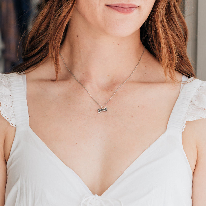 This photo shows the Dog Bone Cremains Memorial Necklace designed and set with ashes by close by me jewelry in Sterling Silver around a red-headed model&
