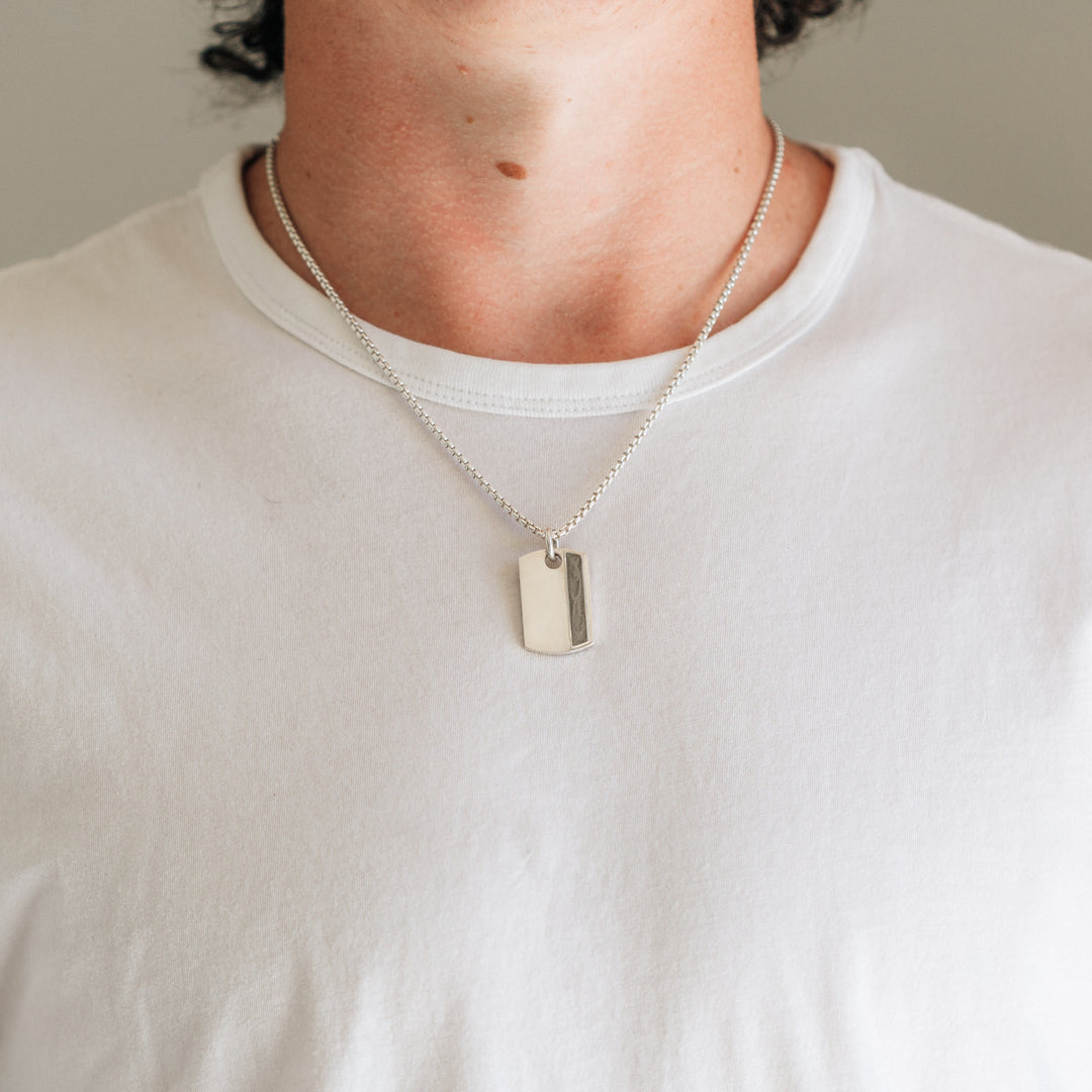A male model in a white shirt wearing the sterling silver dog tag ashes necklace designed by close by me jewelry on a thick chain
