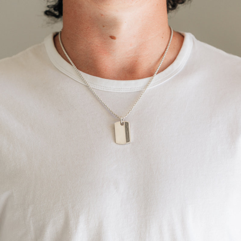 A male model in a white shirt wearing the sterling silver dog tag ashes necklace with ashes designed by close by me jewelry on a thick chain