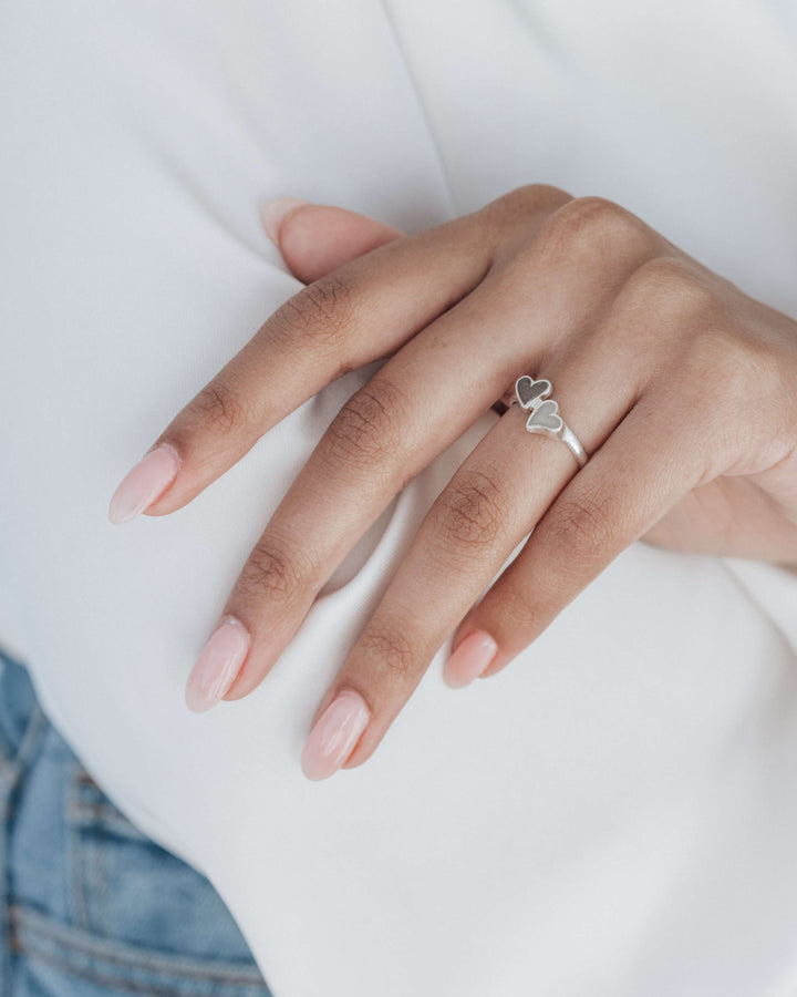 A model showing off her cremation ring with two heart settings in sterling silver while wearing a white blouse