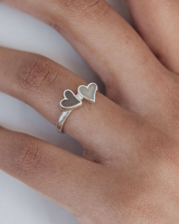 A tight shot of a model's hand as she wears a sterling silver memorial ring with ashes and double heart design