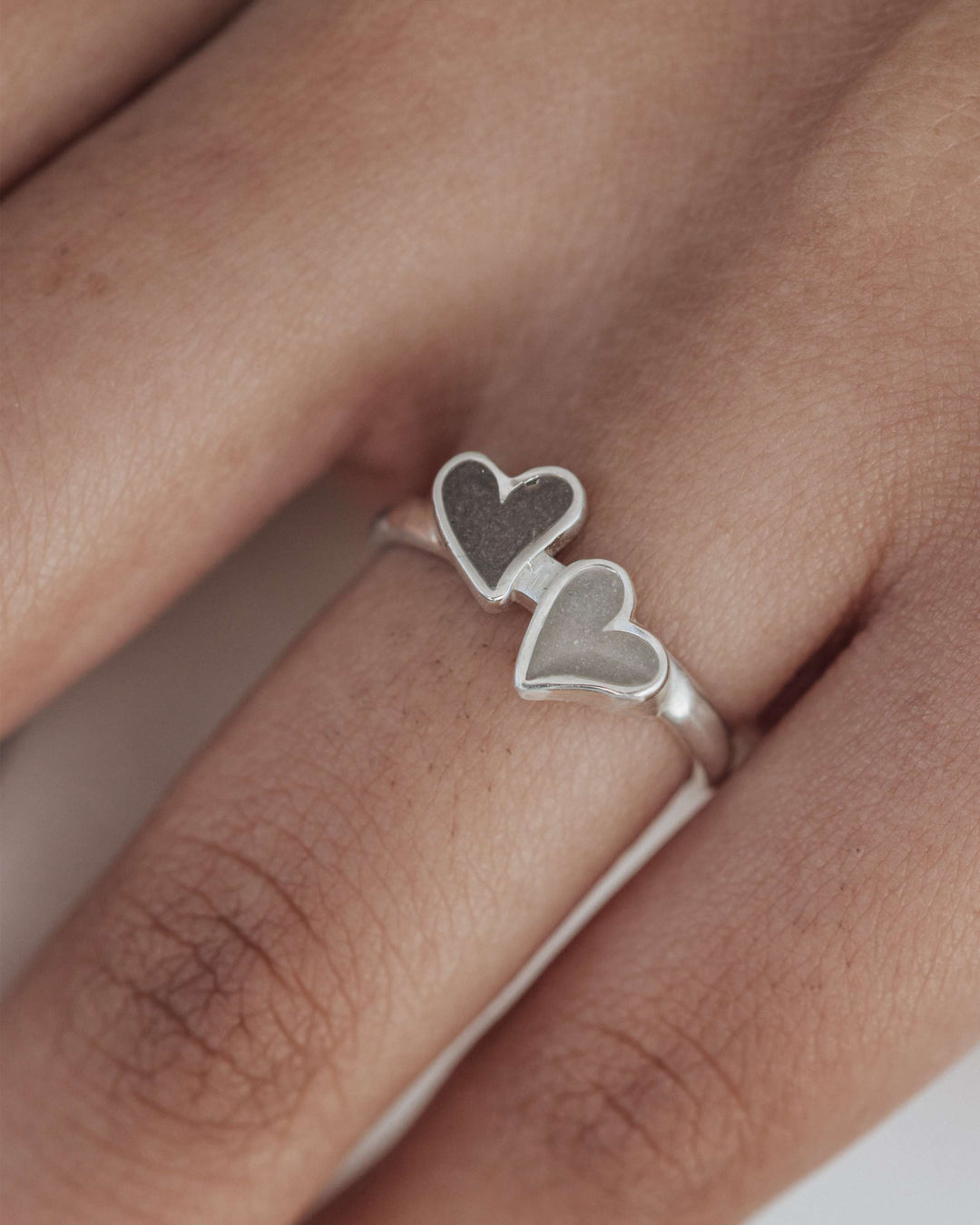 A very close up photo of the sterling silver double heart ashes ring in sterling silver on a model's middle finger