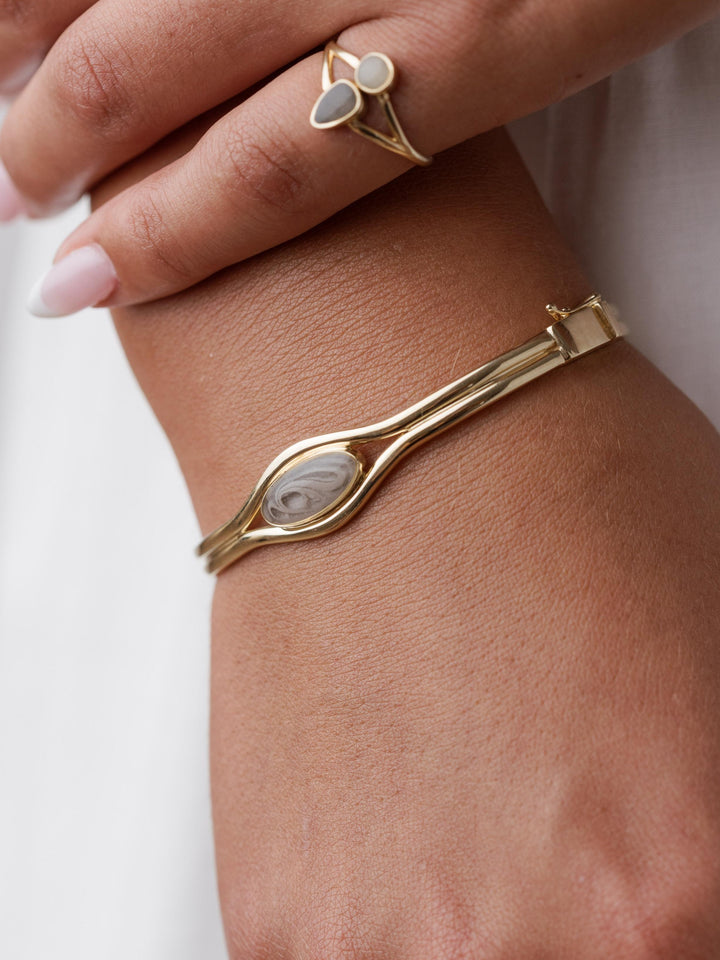 Close-up of the Double Band Oval Bangle Cremation Bracelet on a woman's wrist. Above is the Double Setting Split Shank Cremation Ring on her pinky finger.