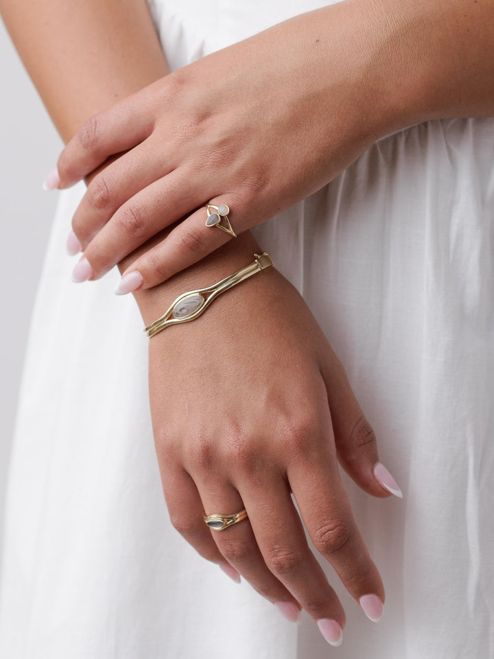 Close-up of a woman wearing the Double Band Oval Bangle Cremation Bracelet on her right wrist, the Double Band Oval Cremation Ring on her right ring finger, and the Double Setting Split Shank Cremation Ring on her left pinky finger.