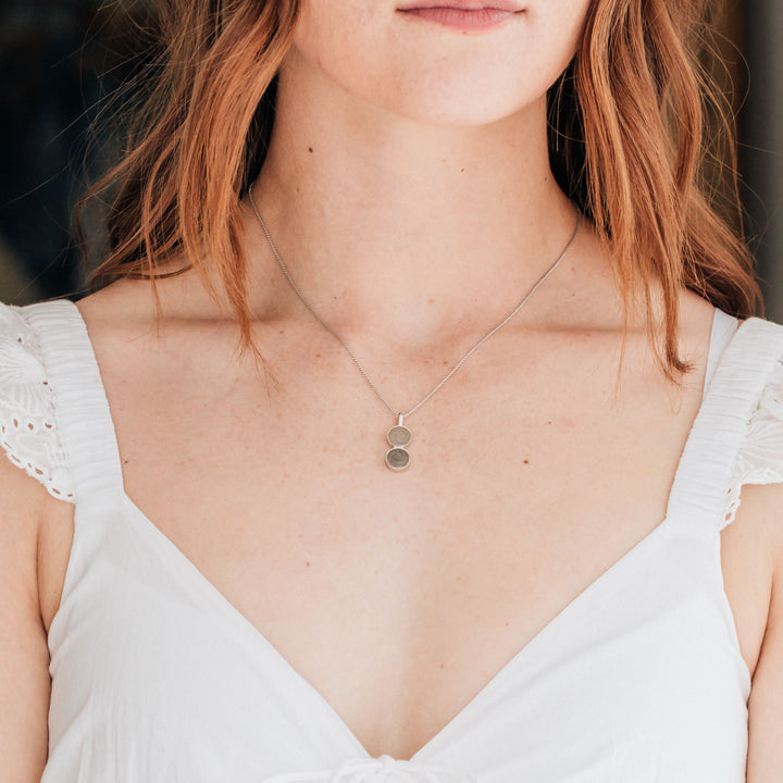 This photo shows a light-skinned model with red hair wearing the Sterling Silver Double Circle Ashes Necklace by close by me jewelry and a white dress