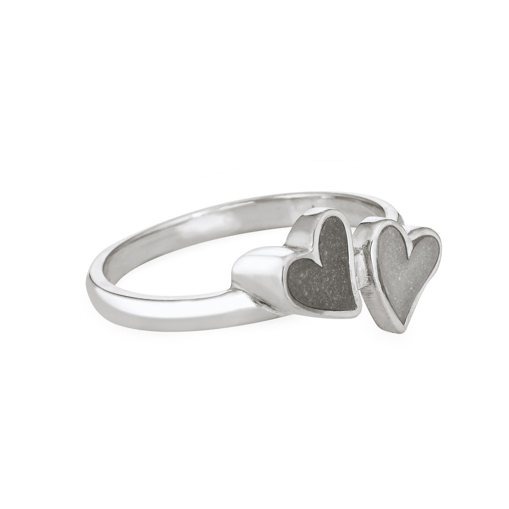 Side view of Close By Me's Sterling Silver Double Heart Cremation Ring, floating against a white backdrop. The left heart has a darker ashes setting, and the right heart has a light grey ashes setting.