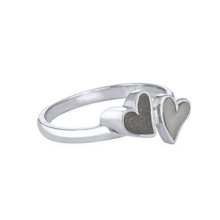 Side view of Close By Me's 14K White Gold Double Heart Cremation Ring, floating against a white backdrop. The left heart has a darker ashes setting, and the right heart has a light grey ashes setting.