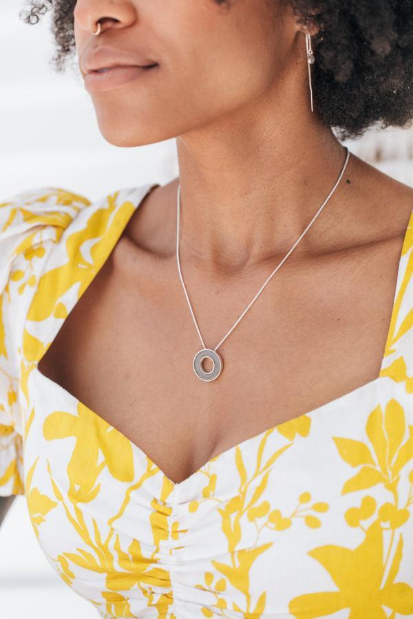 A model in a white and yellow dress with short hair wearing the sterling silver eternity cremation necklace by close by me jewelry