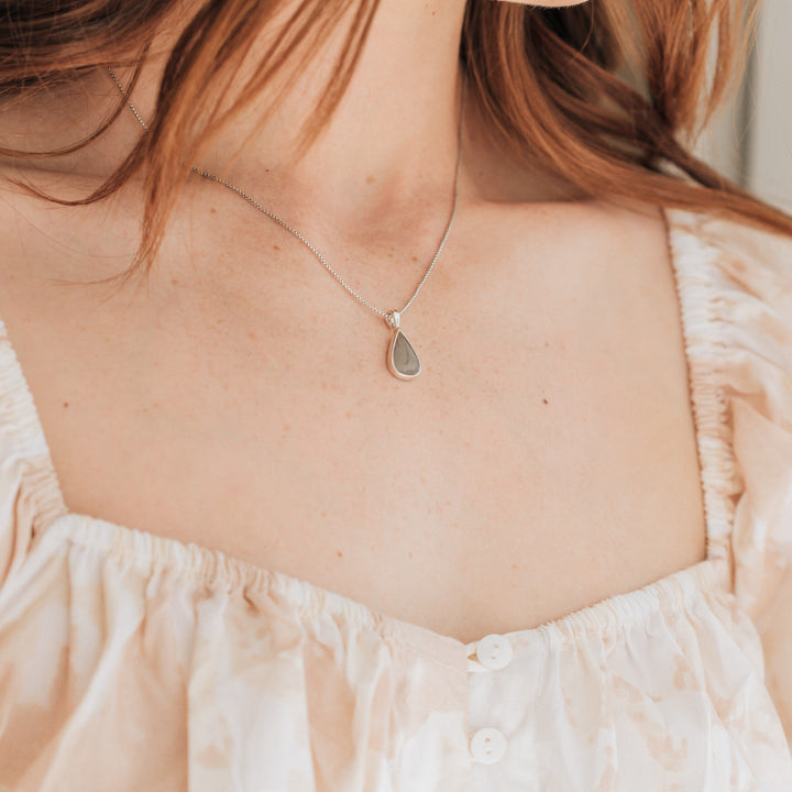 Pictured here is the Sterling Silver Fancy Bail Teardrop Cremains Necklace around a model's neck, designed and set with ashes by close by me jewelry