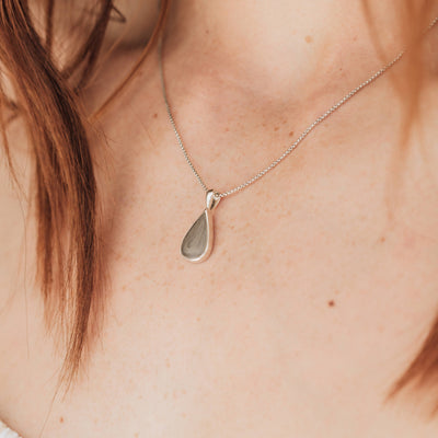 This close up photo shows a model with light skin wearing close by me jewelry's Sterling Silver Fancy Bail Teardrop Memorial Cremated Remains Pendant design