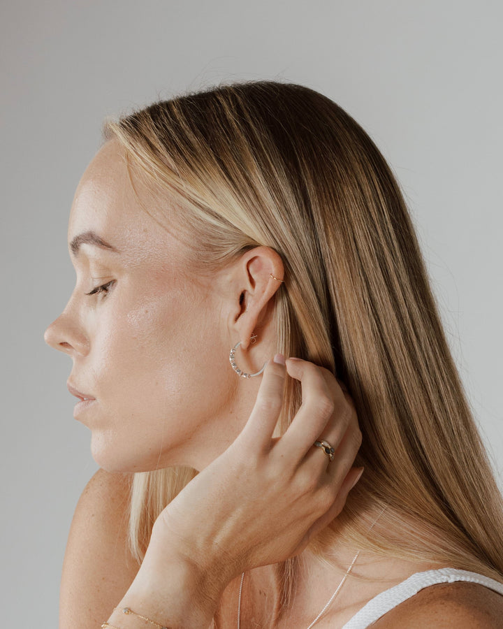 Woman pulls her hair back to reveal Close By Me's Five Setting Open Hoop Cremation Earring in her ear.