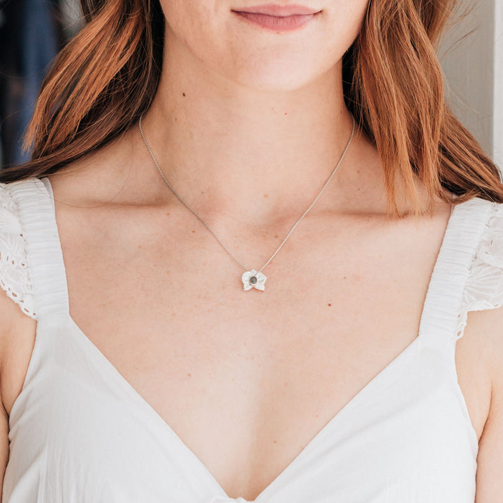 This photo shows a redheaded model in a white dress wearing close by me jewelry's Sterling Silver Hand-Carved Orchid Cremation Necklace