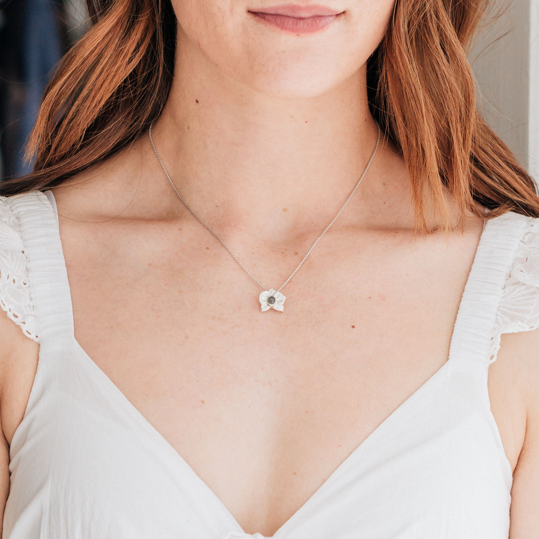 This photo shows a redheaded model in a white dress wearing close by me jewelry's Sterling Silver Hand-Carved Orchid Cremated Remains Pendant