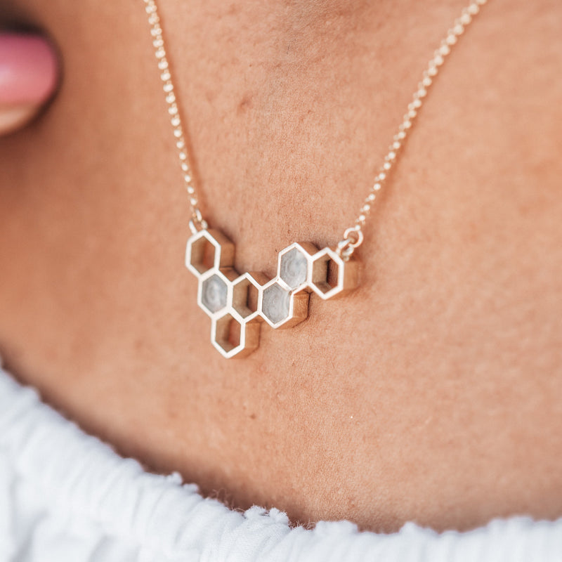 This photo shows a close up of the Hexagon Cremation Cluster Necklace designed and set with cremated remains by close by me jewelry in 14K Yellow Gold being worn by a model in a white top