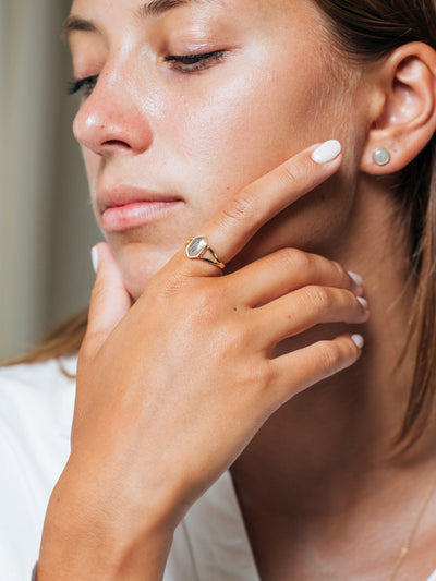 A young, olive skinned woman gazes down with her head turned to the side and hand posed against her face, wearing Close By Me's Hexagon Split Shank Cremation Ring on her index finger.