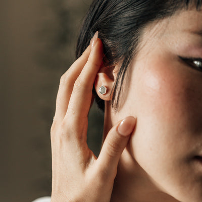 14k white gold hexagon stud ashes earrings pictured on a model with short hair pulling her hair away from her ear in dramatic lighting