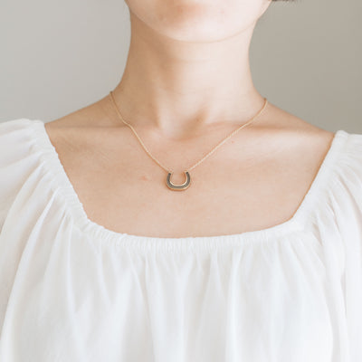 A close-up, cropped photograph of Close By Me's Horseshoe Cremation Necklace being worn around a woman's neck.