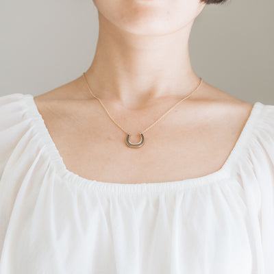 A close-up, cropped photograph of Close By Me's Horseshoe Cremation Necklace being worn around a woman's neck.