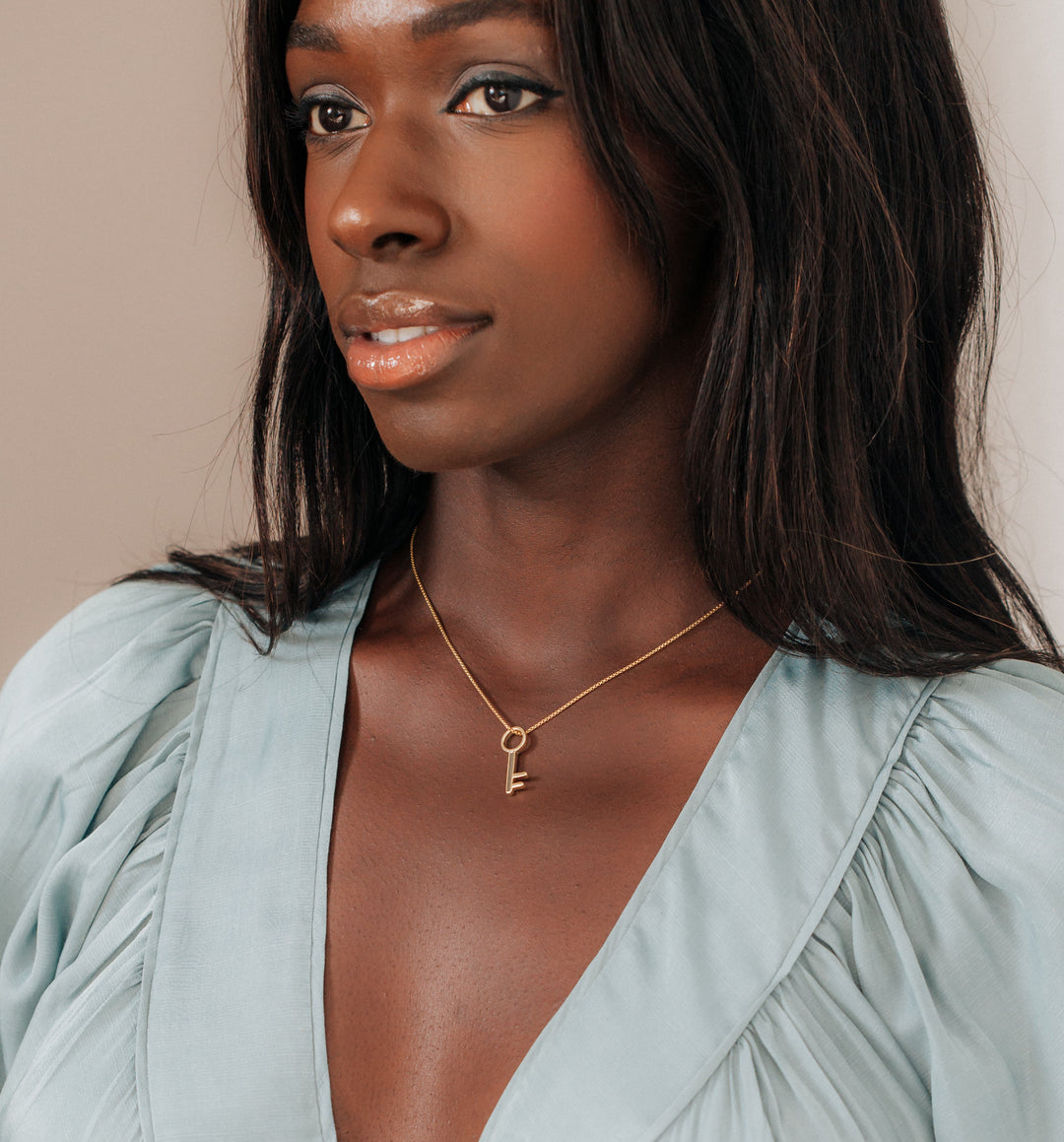 This photo shows a dark skinned model with straight dark hair in a light blue gown wearing close by me jewelry's 14K Yellow Gold Key Necklace with ashes