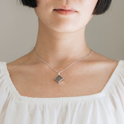 A model wearing close by me jewelry's large luminary pendant with ashes design in sterling silver