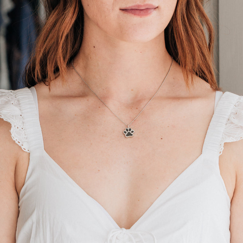 Pictured here is a model in a white dress with auburn hair wearing the Sterling Silver Large Paw Print Cremains Necklace designed by close by me jewelry