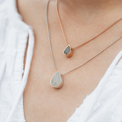 A close up of the Small Pear Sliding Necklace with ashes in 14K Rose Gold and the Large Pear Sliding Cremation Necklace in Sterling Silver by close by me being worn by a light skinned model