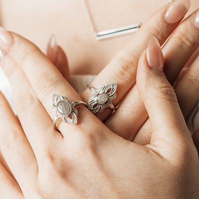 A close-up of a female model's hands crossed against her chest. On her left index finger is Close By Me's Large Setting World War II Cremation Ring; on her right is Close By Me's Small Setting World War II Cremation Ring.