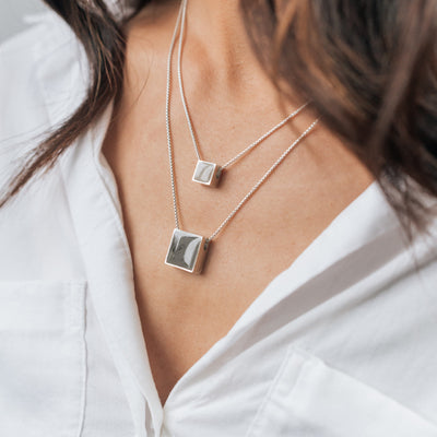A model with tan skin in a white blouse wearing close by me's Sterling Silver Memorial Sliding Pendants, one with a Small Square Setting and one with a Large Square Setting