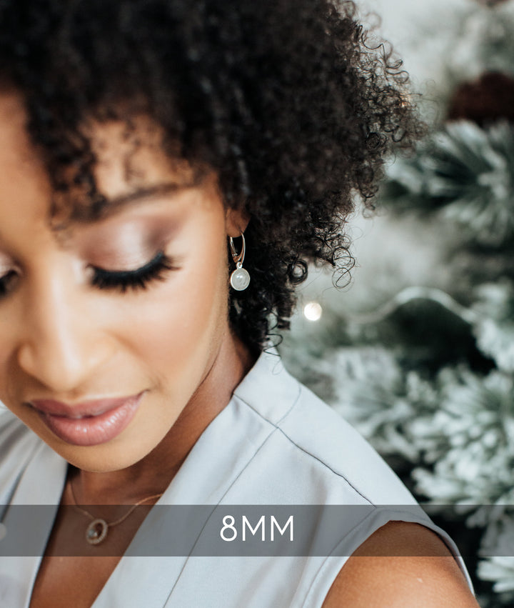 A curly haired, dark skinned model is gazing down, with Close By Me's Lever-Back Dome Cremation Earring visible in her left ear. A banner towards the bottom of the picture says "8MM".
