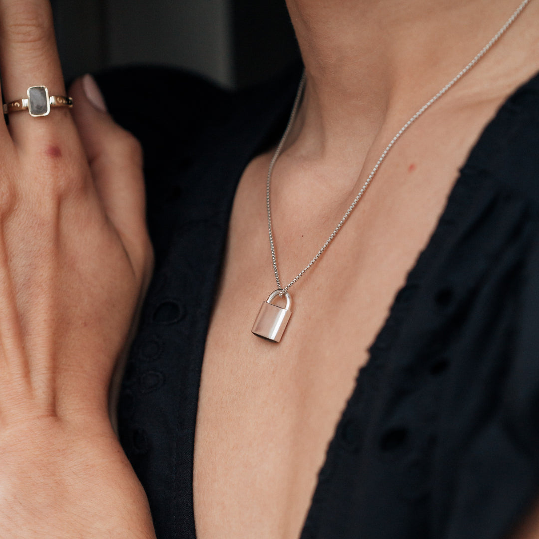 A close up of a model in a black dress wearing close by me jewelry's Sterling Silver Lock Pendant with cremated remains on a standard rounded box chain