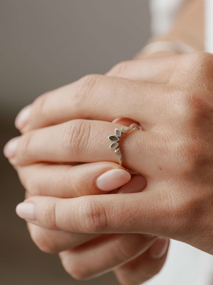 Close By Me's Lotus Cremation Ring in Sterling Silver on the ring finger of a female model's left hand. The thumb and index finger of her right hand are gently holding either side of the finger wearing the ring.