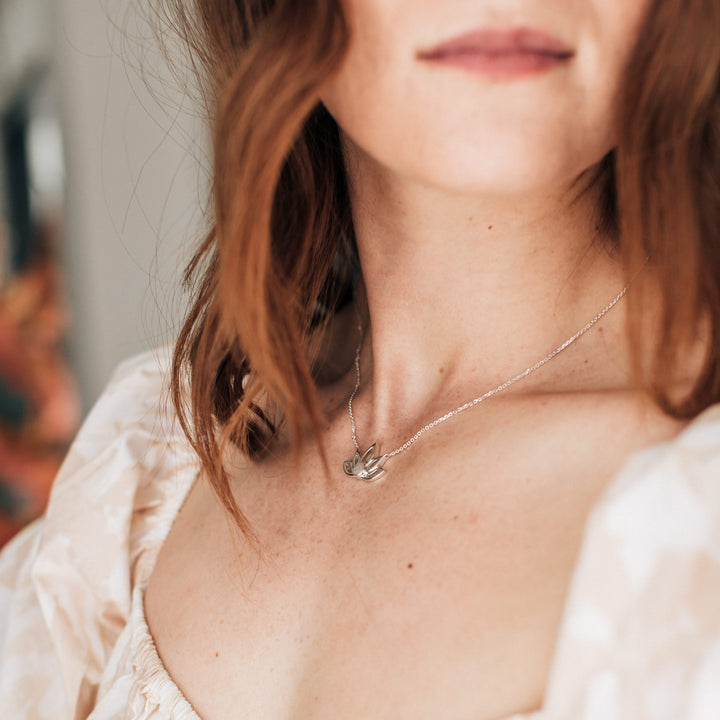 Pictured here is the Sterling Silver Lotus Flower Cremation Necklace in Sterling Silver being worn by a red-headed model in a peach dress at an angle