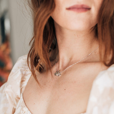 Pictured here is the Sterling Silver Lotus Flower Necklace with Cremains in Sterling Silver being worn by a red-headed model in a peach dress at an angle